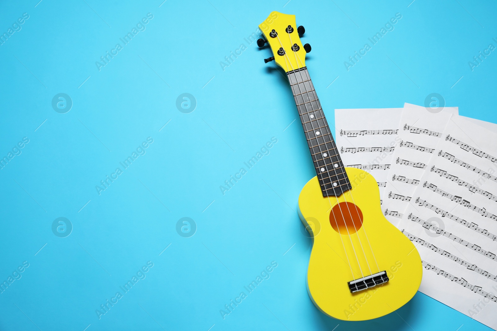 Photo of Ukulele and music sheets on light blue background, top view. Space for text