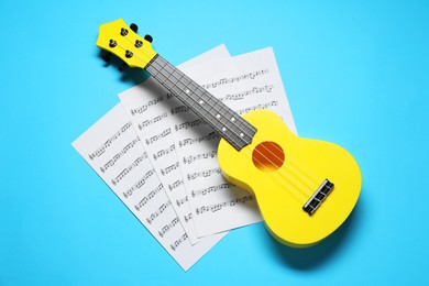 Photo of Ukulele and music sheets on light blue background, top view