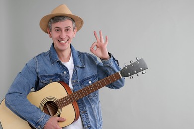 Photo of Happy man with guitar showing okay gesture on light grey background. Space for text