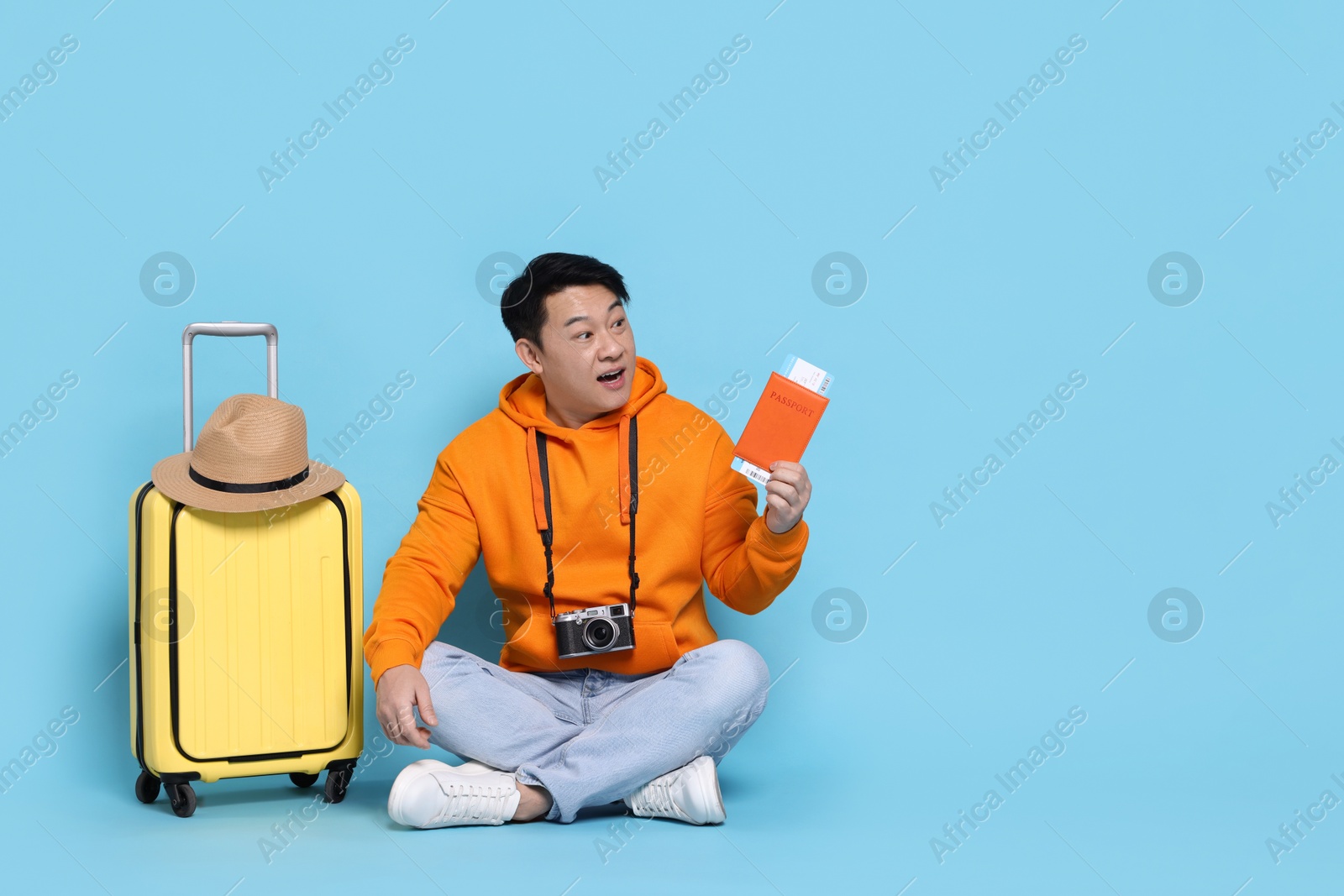 Photo of Traveller with passport, camera and suitcase on light blue background. Space for text