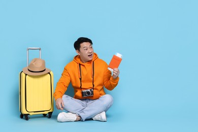 Photo of Traveller with passport, camera and suitcase on light blue background. Space for text