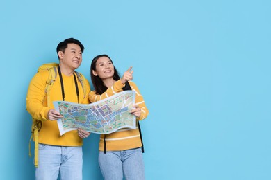 Photo of Happy travellers with map pointing at something on light blue background. Space for text