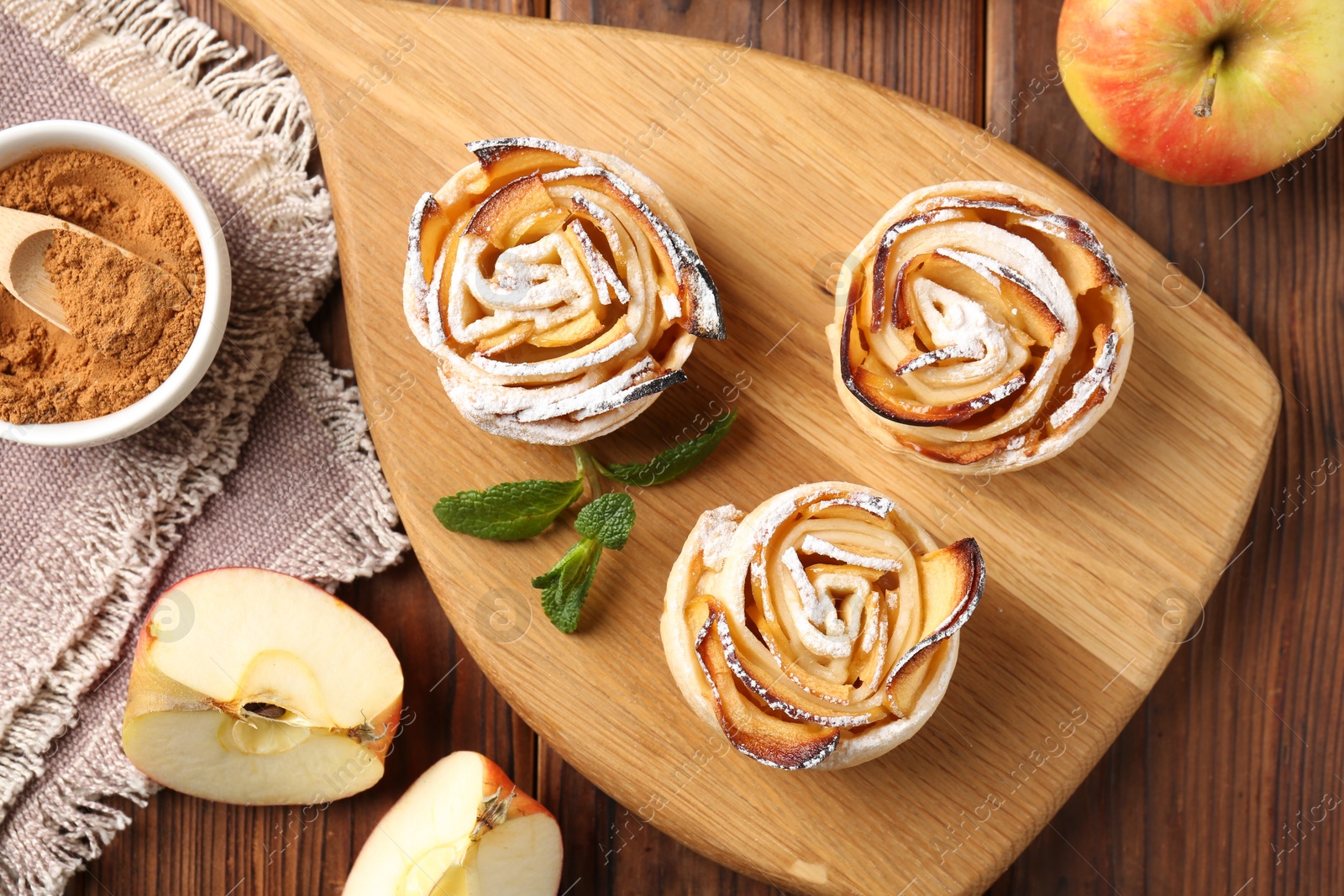 Photo of Tasty apple roses with powdered sugar served on wooden table, flat lay