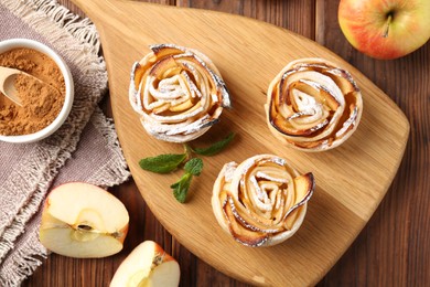 Photo of Tasty apple roses with powdered sugar served on wooden table, flat lay