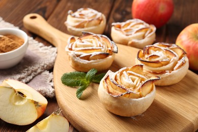 Photo of Tasty apple roses with powdered sugar served on wooden table, closeup