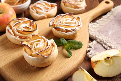 Photo of Tasty apple roses with powdered sugar served on wooden table, closeup