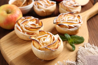 Photo of Tasty apple roses with powdered sugar served on wooden table, closeup