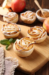Photo of Tasty apple roses with powdered sugar served on wooden table, closeup