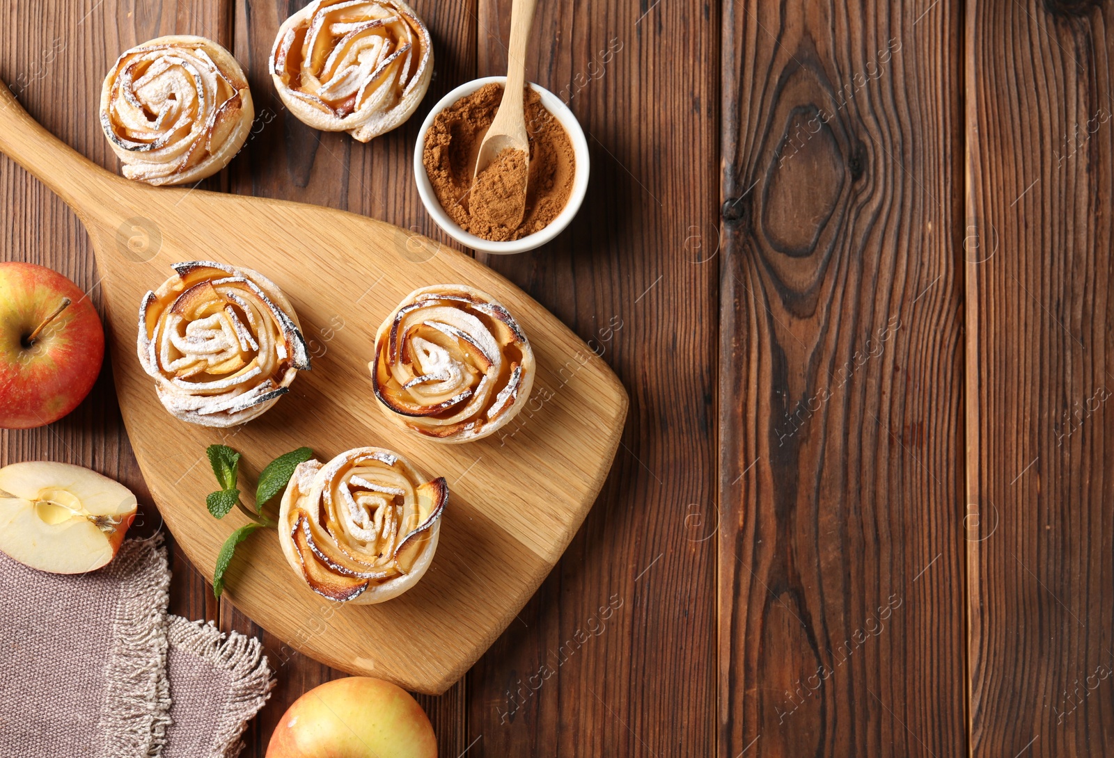 Photo of Tasty apple roses with powdered sugar served on wooden table, flat lay. Space for text