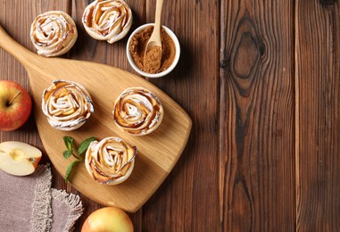Photo of Tasty apple roses with powdered sugar served on wooden table, flat lay. Space for text