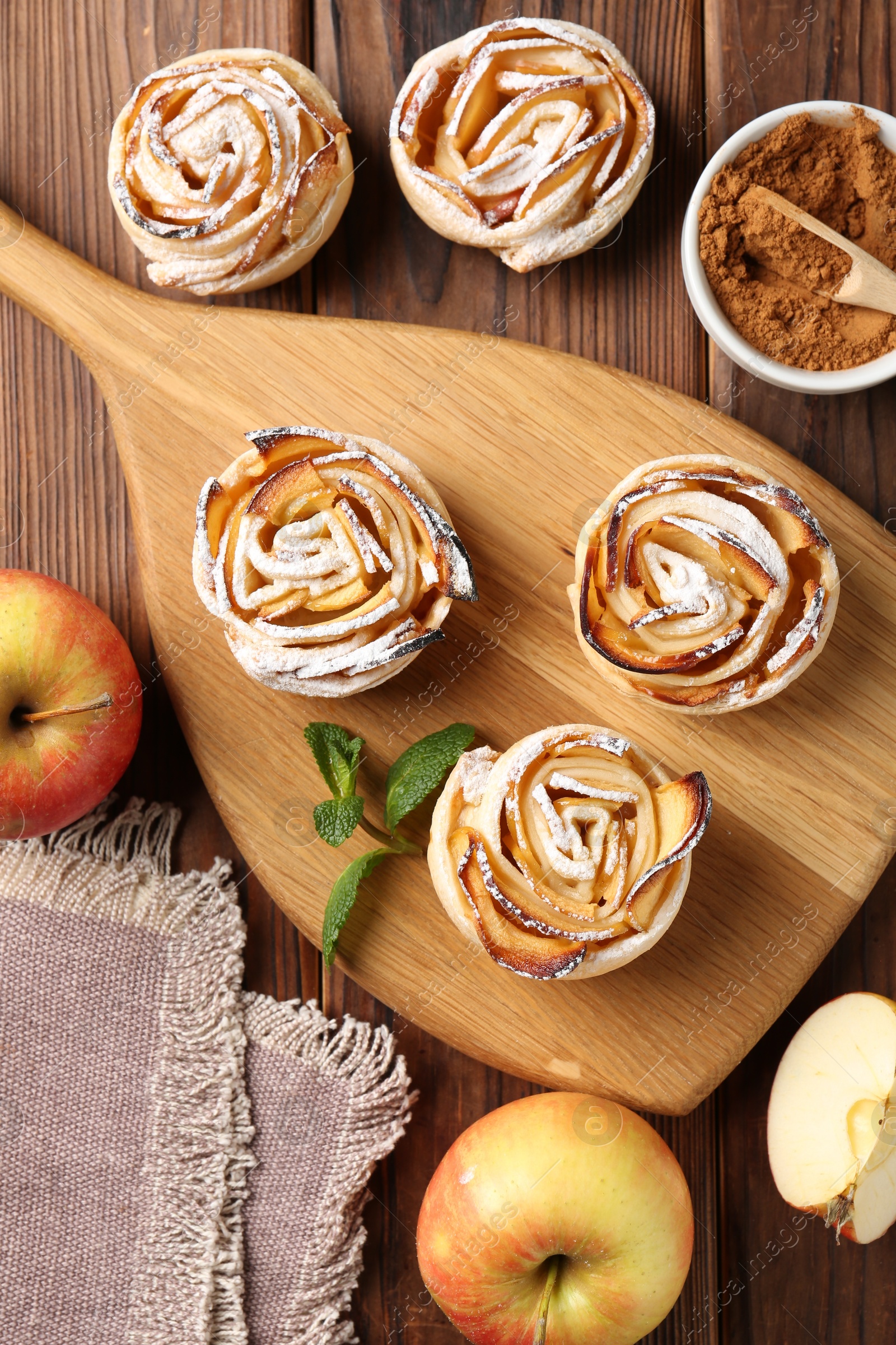 Tasty apple roses with powdered sugar served on wooden table, flat lay Photo of Tasty apple roses with powdered sugar served on wooden table, flat lay