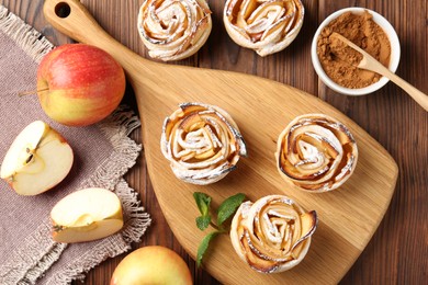 Photo of Tasty apple roses with powdered sugar served on wooden table, flat lay