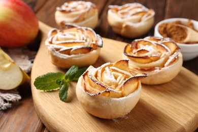 Photo of Tasty apple roses with powdered sugar served on wooden table, closeup