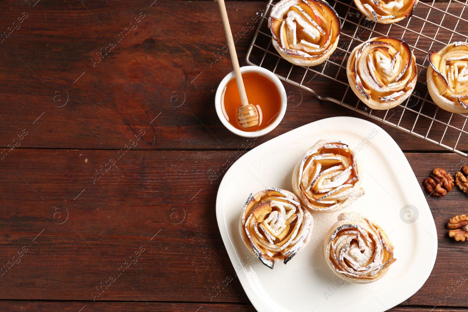 Photo of Tasty apple roses with powdered sugar served on wooden table, flat lay. Space for text