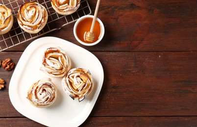 Photo of Tasty apple roses with powdered sugar served on wooden table, flat lay. Space for text