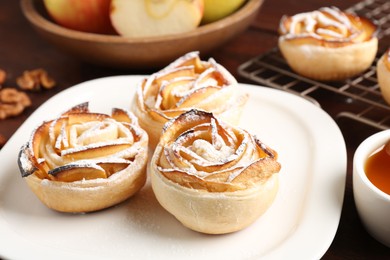 Photo of Tasty apple roses with powdered sugar served on wooden table, closeup