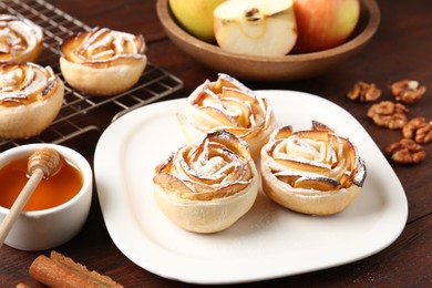 Photo of Tasty apple roses with powdered sugar served on wooden table, closeup