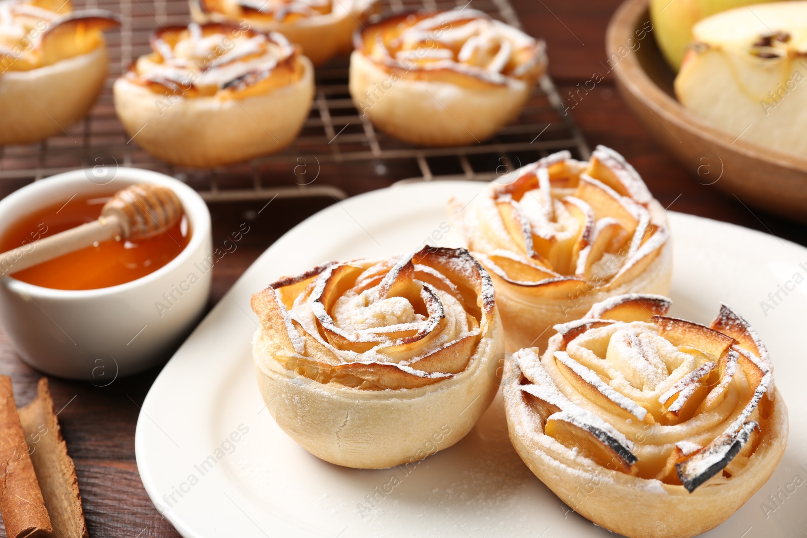 Photo of Tasty apple roses with powdered sugar served on wooden table, closeup