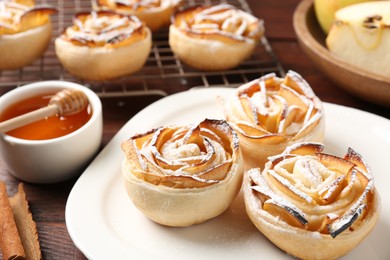 Photo of Tasty apple roses with powdered sugar served on wooden table, closeup