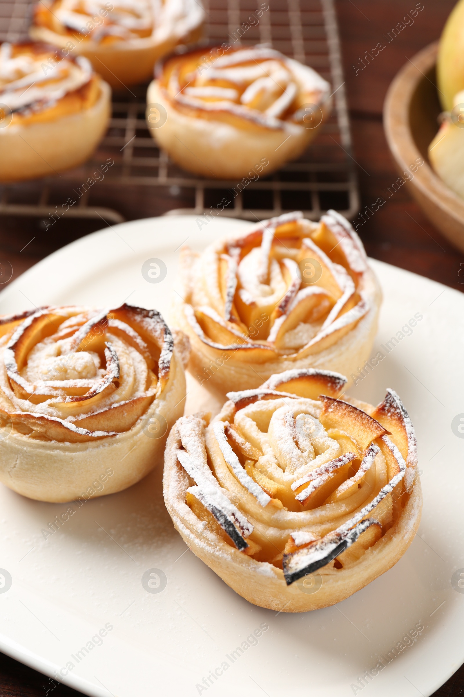 Photo of Tasty apple roses with powdered sugar served on wooden table, closeup