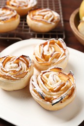 Photo of Tasty apple roses with powdered sugar served on wooden table, closeup