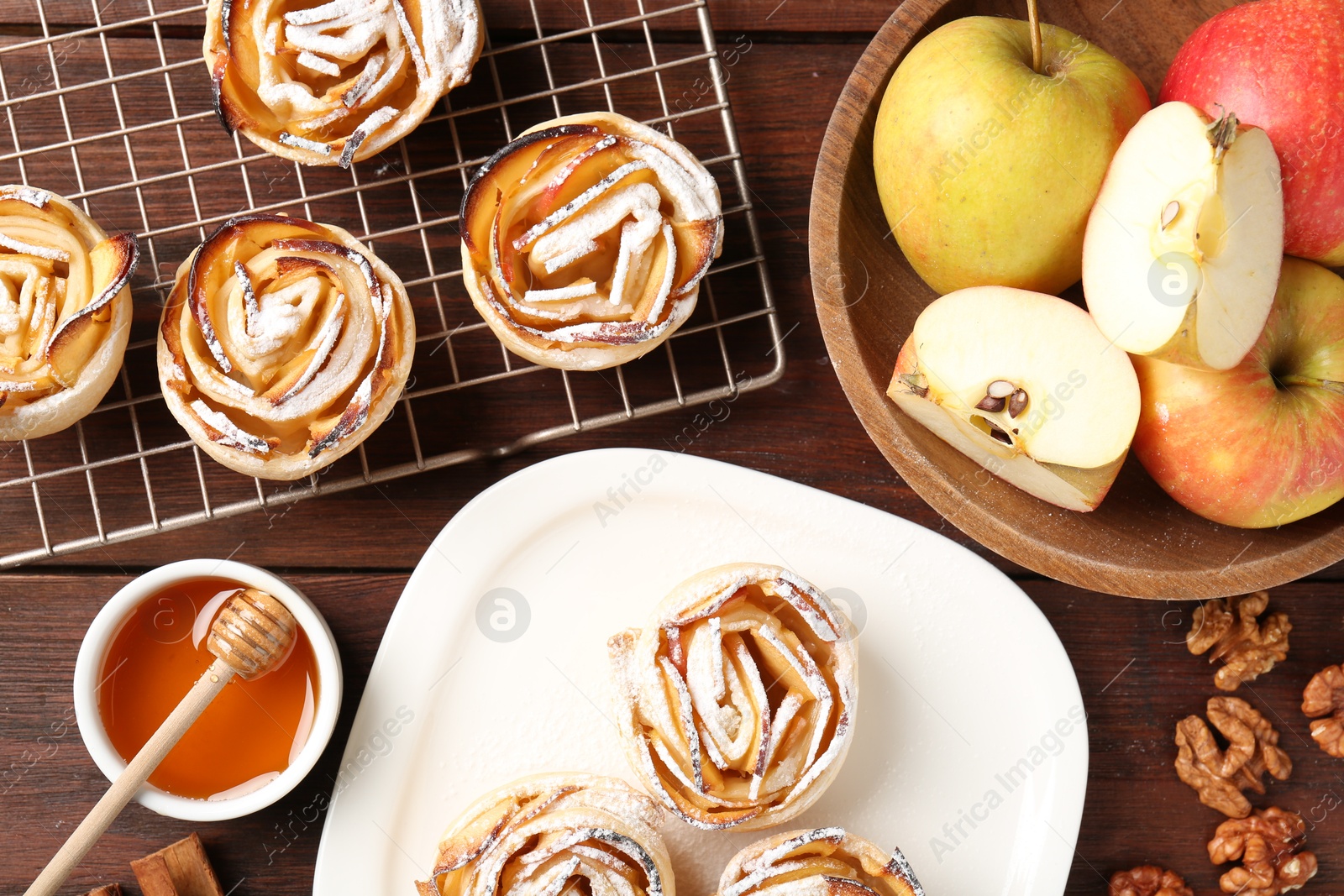 Photo of Tasty apple roses with powdered sugar served on wooden table, flat lay