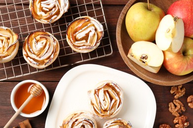 Photo of Tasty apple roses with powdered sugar served on wooden table, flat lay
