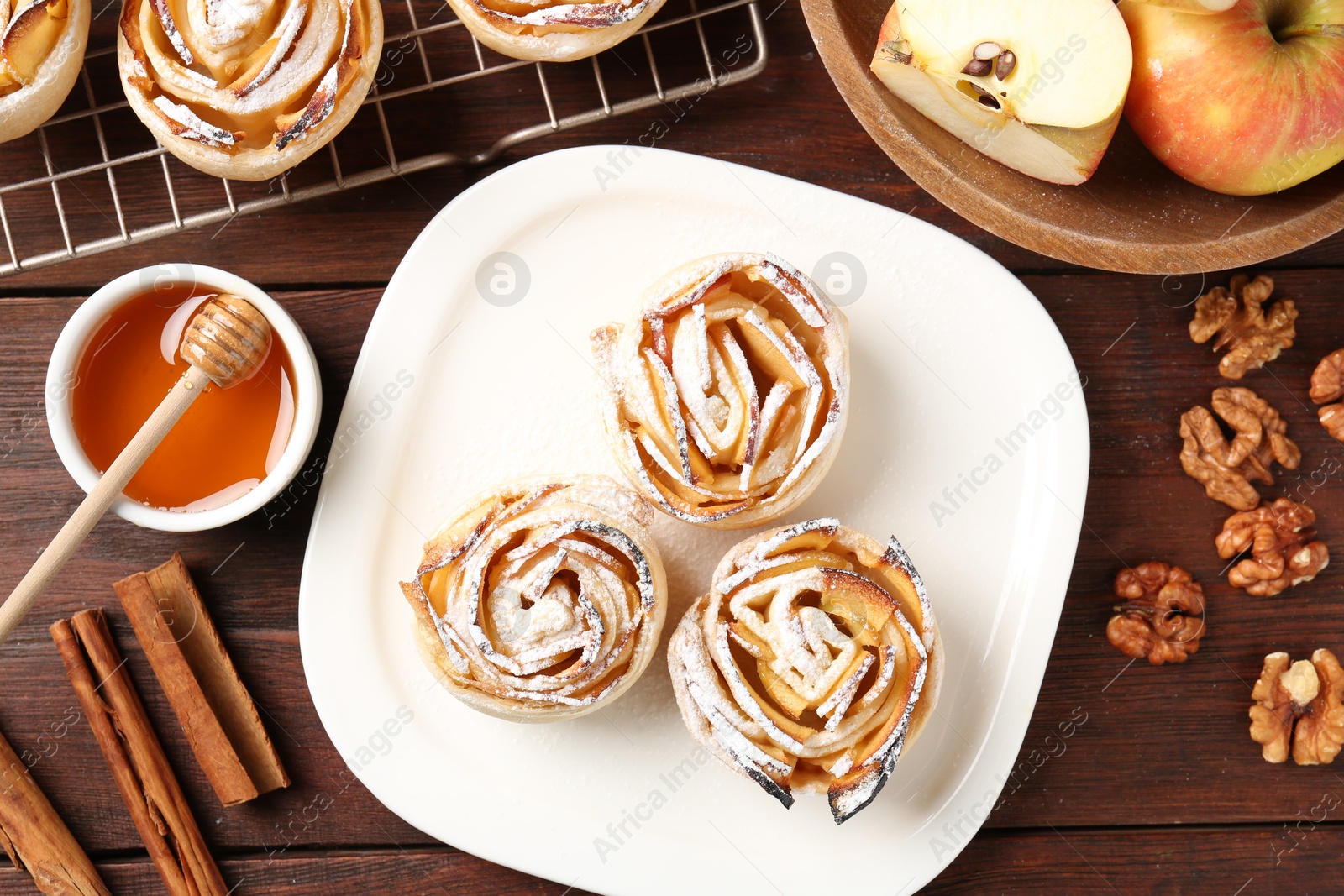 Photo of Tasty apple roses with powdered sugar served on wooden table, flat lay