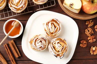 Photo of Tasty apple roses with powdered sugar served on wooden table, flat lay