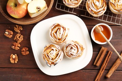 Photo of Tasty apple roses with powdered sugar served on wooden table, flat lay