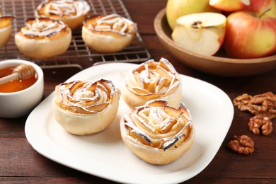 Photo of Tasty apple roses with powdered sugar served on wooden table, closeup