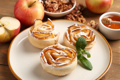 Photo of Tasty apple roses with powdered sugar served on wooden table, closeup