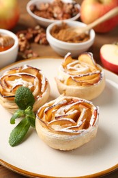Photo of Tasty apple roses with powdered sugar served on table, closeup