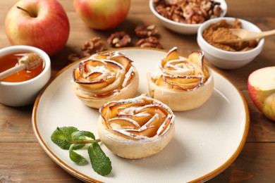 Photo of Tasty apple roses with powdered sugar served on wooden table, closeup