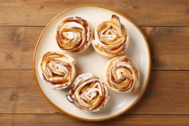 Photo of Tasty apple roses with powdered sugar on wooden table, top view