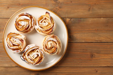 Photo of Tasty apple roses with powdered sugar on wooden table, top view. Space for text