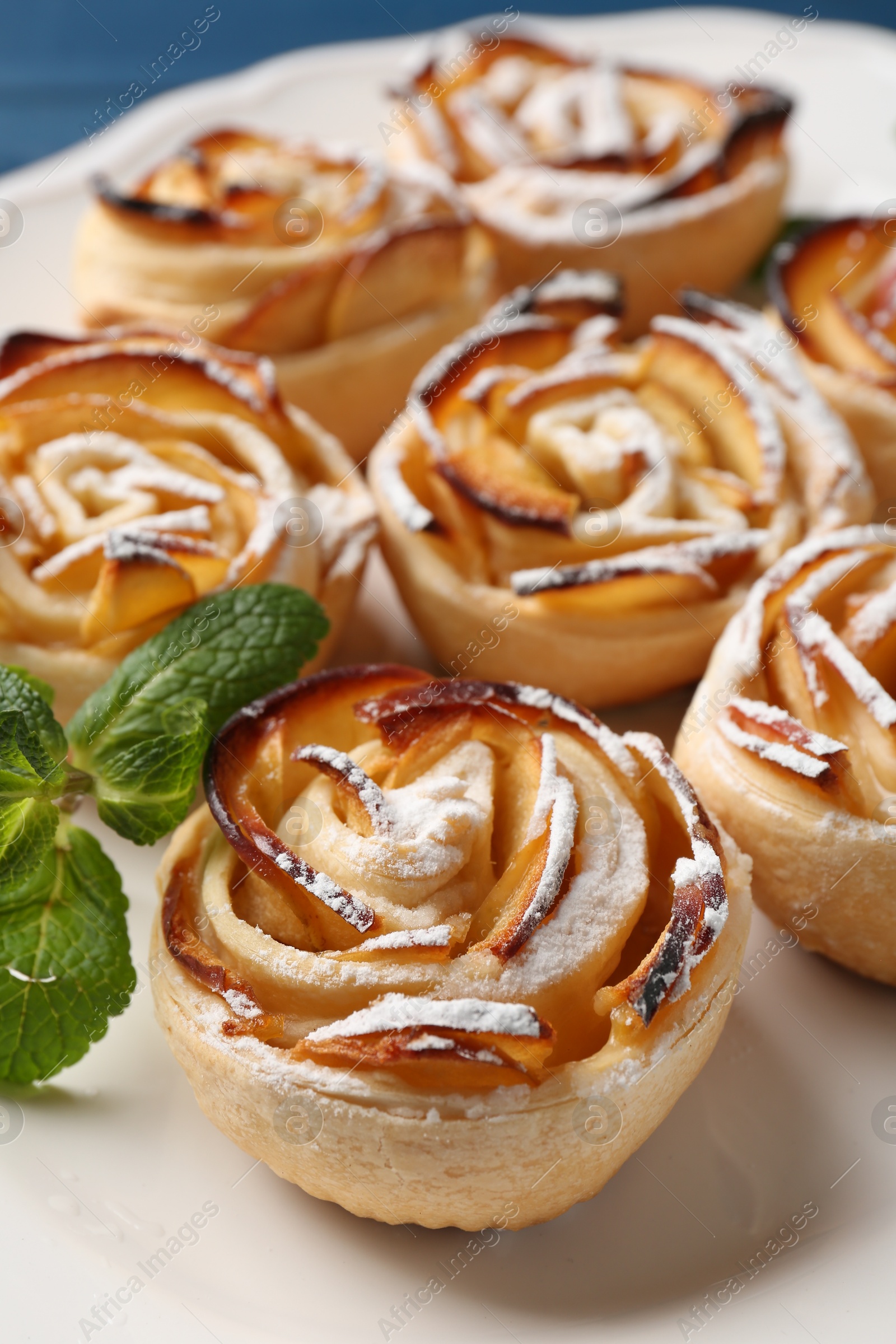 Photo of Tasty apple roses with powdered sugar served on table, closeup