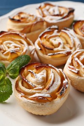 Photo of Tasty apple roses with powdered sugar served on table, closeup