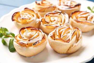 Photo of Tasty apple roses with powdered sugar served on blue table, closeup