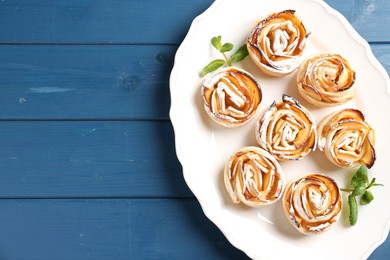 Photo of Tasty apple roses with powdered sugar served on blue wooden table, top view