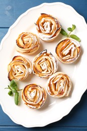 Photo of Tasty apple roses with powdered sugar served on blue wooden table, top view