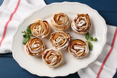 Photo of Tasty apple roses with powdered sugar served on blue wooden table, top view