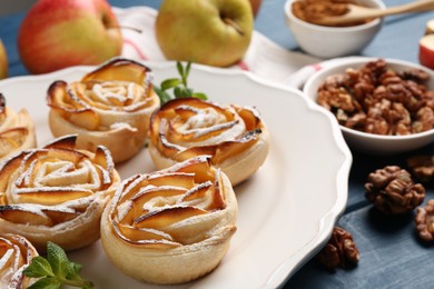 Photo of Tasty apple roses with powdered sugar served on blue wooden table, closeup