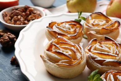 Photo of Tasty apple roses with powdered sugar served on blue wooden table, closeup