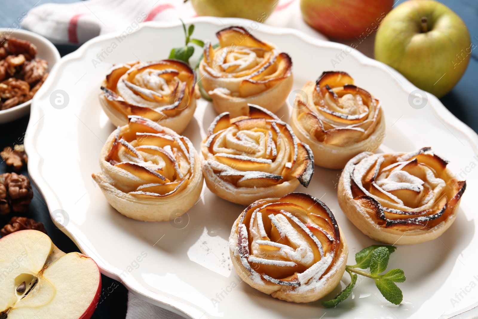 Photo of Tasty apple roses with powdered sugar served on table, closeup