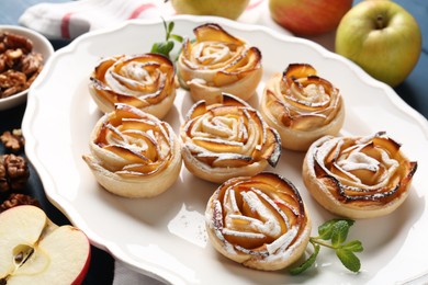 Photo of Tasty apple roses with powdered sugar served on table, closeup