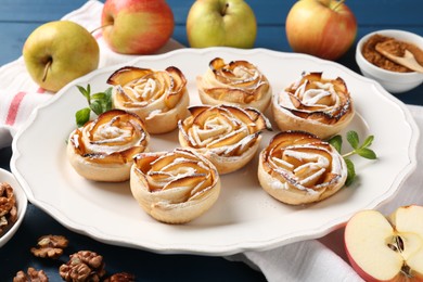 Photo of Tasty apple roses with powdered sugar served on blue wooden table, closeup