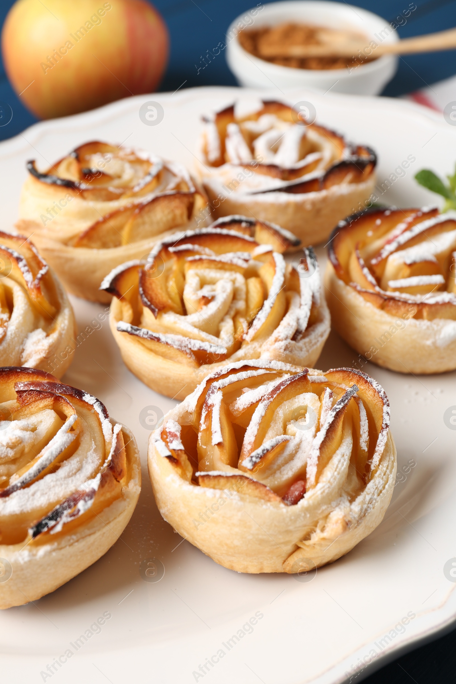 Photo of Tasty apple roses with powdered sugar served on table, closeup