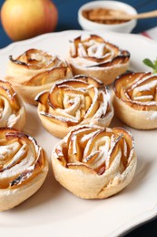 Photo of Tasty apple roses with powdered sugar served on table, closeup