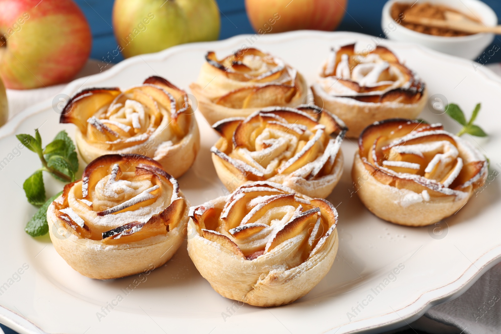 Photo of Tasty apple roses with powdered sugar served on table, closeup